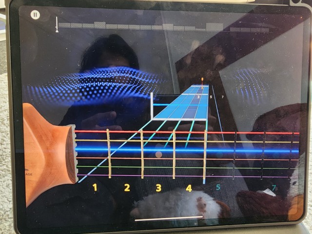 iPad showing Rocksmith+ gameplay with color-coded note highway on the virtual fretboard